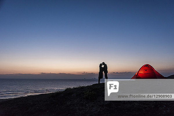 Romantic couple camping on the beach  kissing in twilight