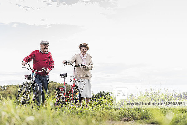Senior couple pushing bicycles in rural landscape