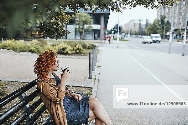 Young woman sitting on a bench  drinking coffee