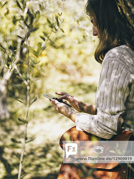 Italy  woman leaning against olive tree using cell phone