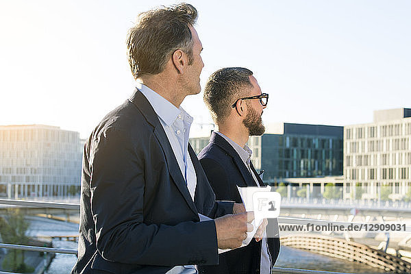 Two businessmen on a bridge in the city looking around