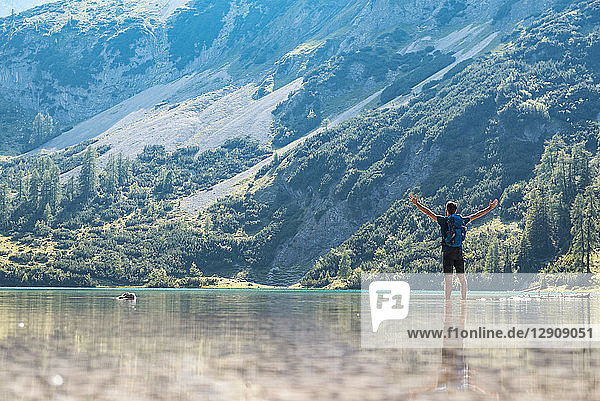 Austria  Tyrol  Hiker at Lake Seebensee standing ankle deep in water  with raised arms