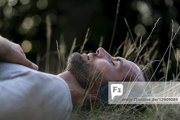 Relaxed man lying in field listening to music with headphones