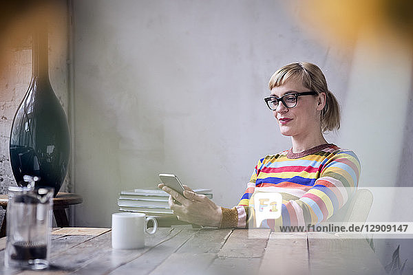 Portrait of smiling woman sitting at table with cup of coffee looking at cell phone