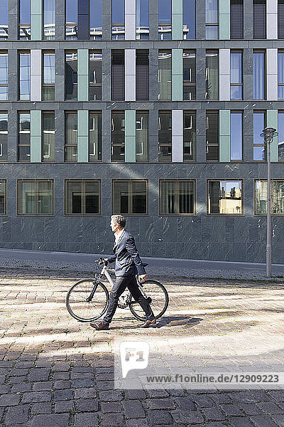 Mature businessman pushing bicycle in the city