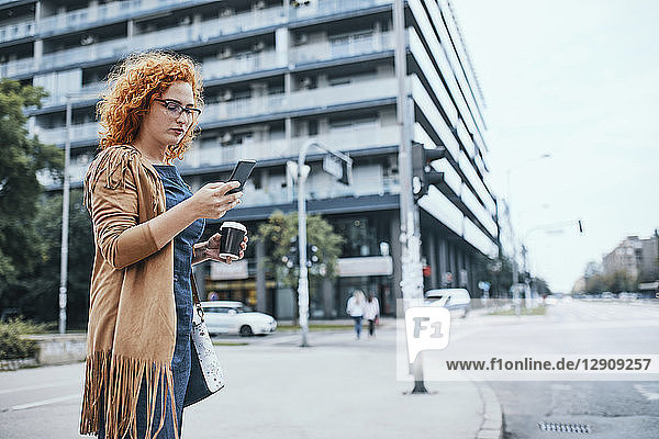 Young woman waiting to cross road  using smartphone