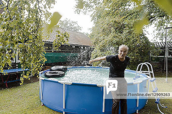 Portrait of carefree mature man enjoying summer rain at swimming pool in garden