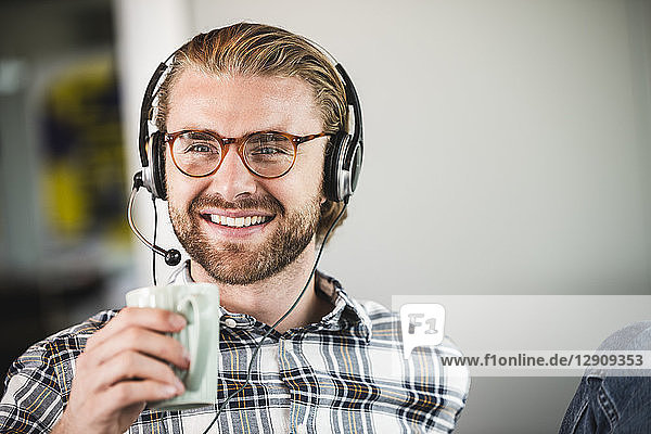 Portrait of smiling casual businessman with cup of coffee and headset