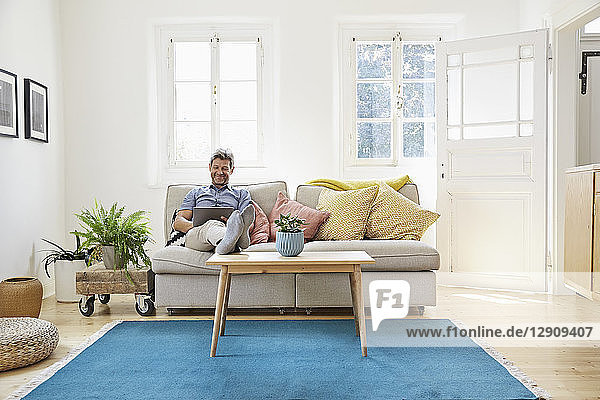 Man sitting on couch at home  using digital tablet