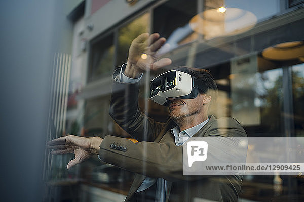Mature businessman sitting in coffee shop  looking through VR glasses
