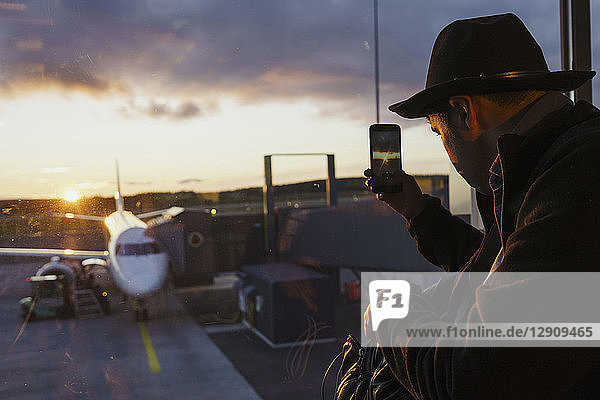 Young man behind window taking cell phone picture of plane at the airport