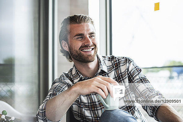 Portrait of smiling businessman with cup of coffee in office