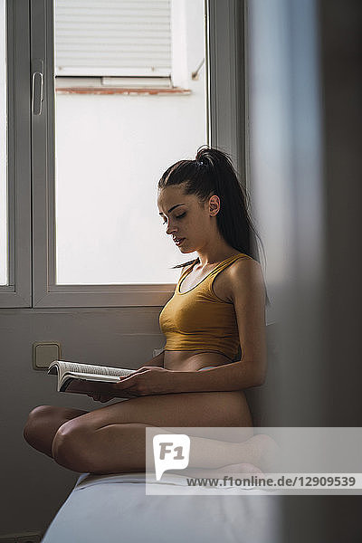Beautiful young woman in underwear reading a book at home