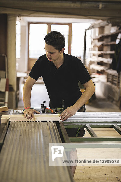 Carpenter sawing piece of wood in workshop