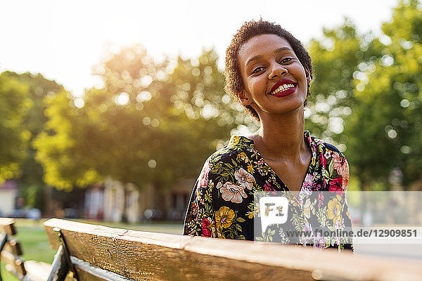 Portrait of smiling young woman on bench in a park