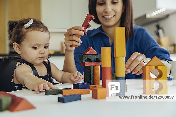 Happy mother and baby daughter playing with building blocks