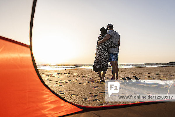 Romantic couple camping on the beach  embracing at sunset