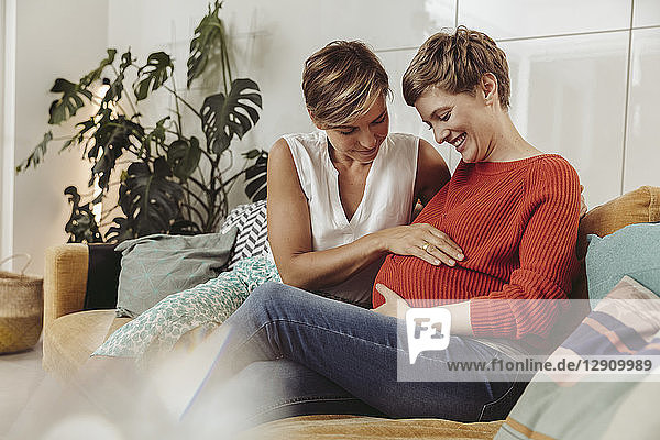 Happy lesbian couple touching belly of the expectant mother