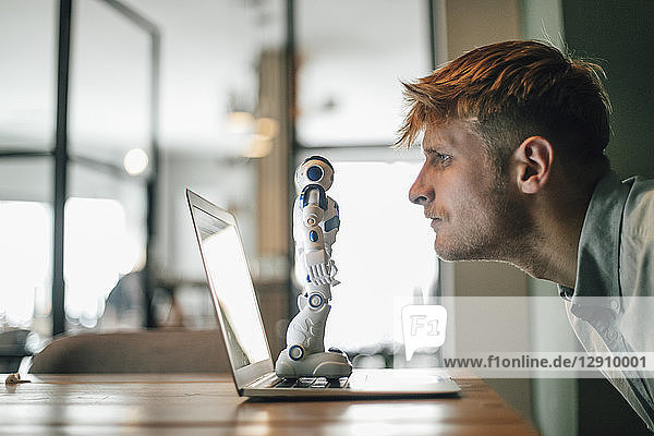 Man looking at toy robot  standing on his laptop