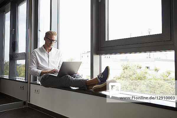 Businessman sitting on windowsill using laptop