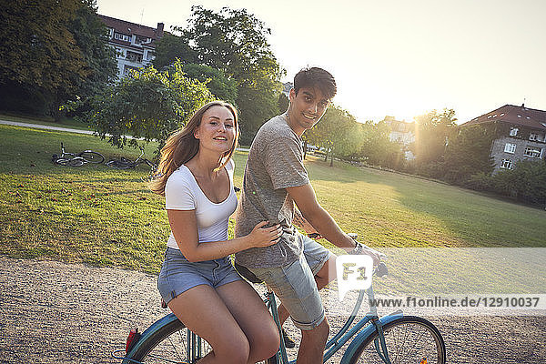 Young couple riding bicycle in park  woman sitting on rack
