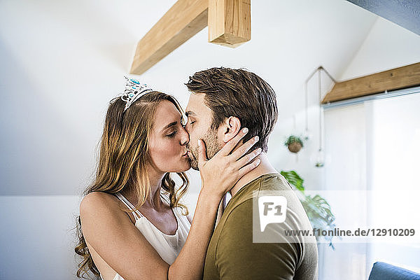 Affectionate couple kissing at home with woman wearing tiara