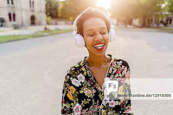 Happy fashionable young woman with headphones outdoors at sunset