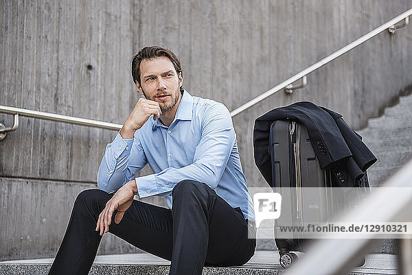 Businessman with rolling suitcase sitting on stairs