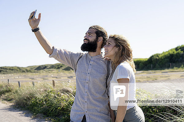 Young couple taking smartphone selfies on the beach