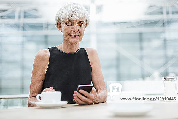 Senior woman using cell phone in a cafe