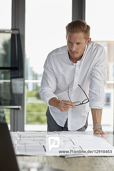 Young man working on blueprint on desk in office