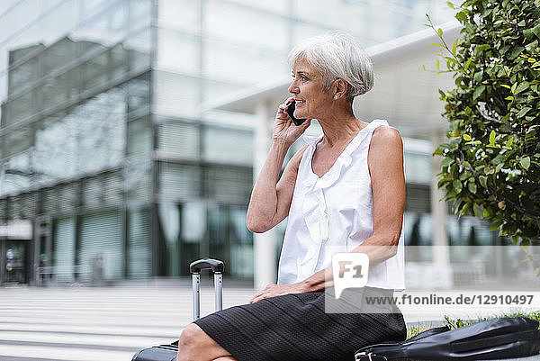 Smiling senior woman with baggage on cell phone in the city