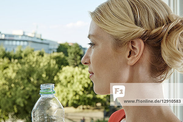 Young woman with water bottle at the window looking out
