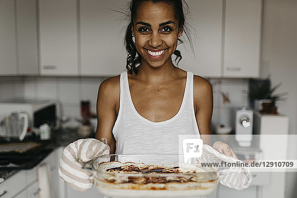 Portrait of smiling young woman with casserole in the kitchen