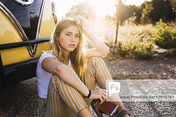 Young woman holding vintage camera sitting outside at a van