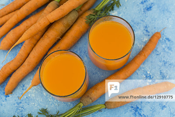 Two glasses of fresh carrot juice and carrots on light blue ground