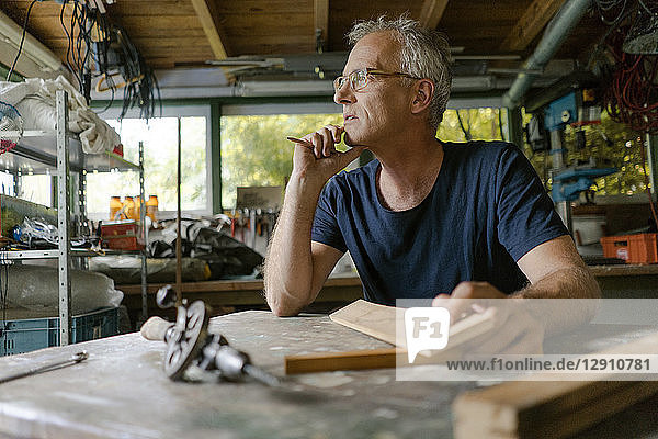 Mature man at workbench in his workshop thinking