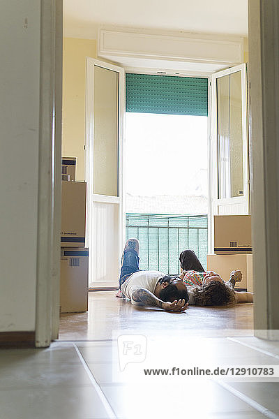 Couple lying side by side on the floor of new home in front of open balcony door