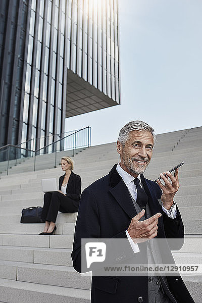 Portrait of businessman talking on mobile phone while business woman working on laptop in the background