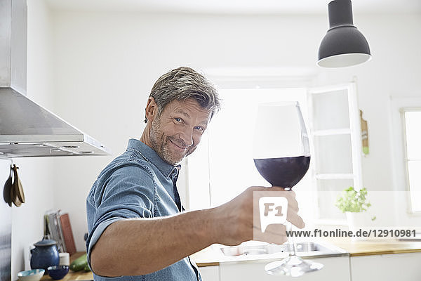 Man in kitchen toasting with glass of red wine