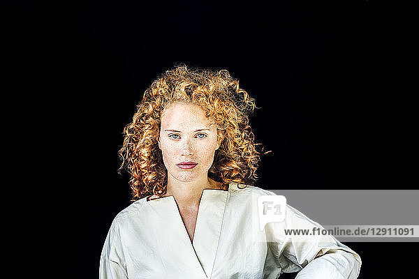 Portrait of serious young woman with curly red hair in front of black background