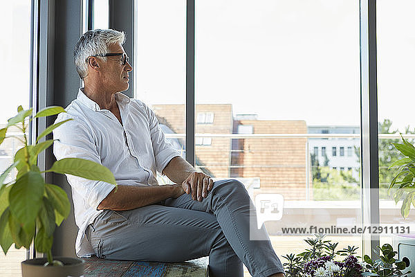 Pensive mature man sitting at the window at home