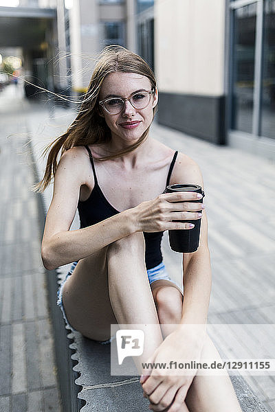 Young woman sitting on a wall  drinking coffee to go