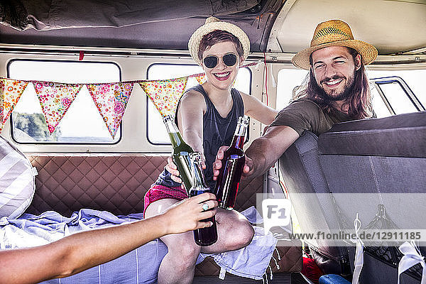 Happy friends inside van clinking bottles