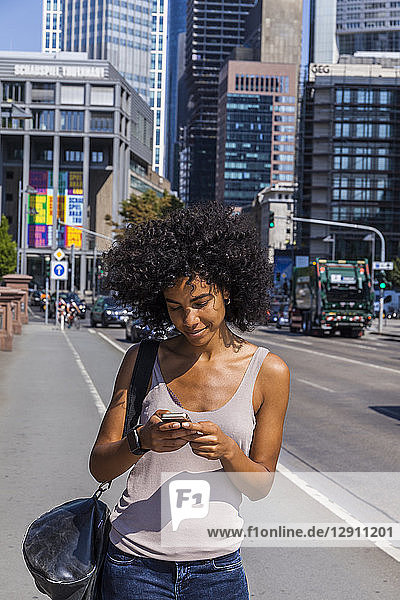 Germany  Frankfurt  smiling young woman with curly hair using cell phone
