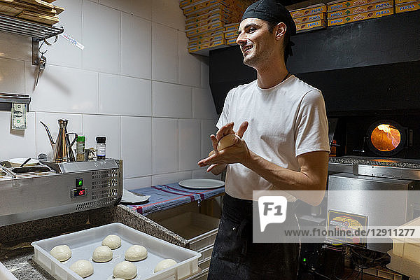 Smiling pizza baker shaping dough in kitchen