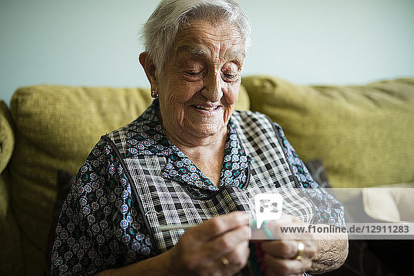 Portrait of smiling senior woman crocheting on the couch at home