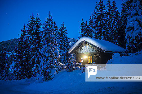 Austria,  Altenmarkt-Zauchensee,  sledges,  snowman and Christmas tree at illuminated wooden house in snow at night