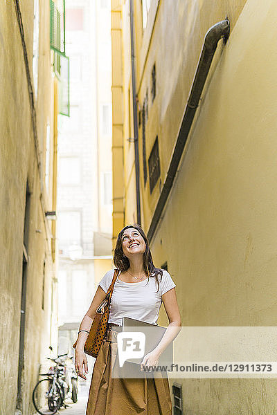 Smiling woman walking in an alley carrying laptop