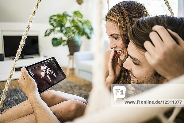 Happy affectionate couple looking at ultrasound scan on tablet